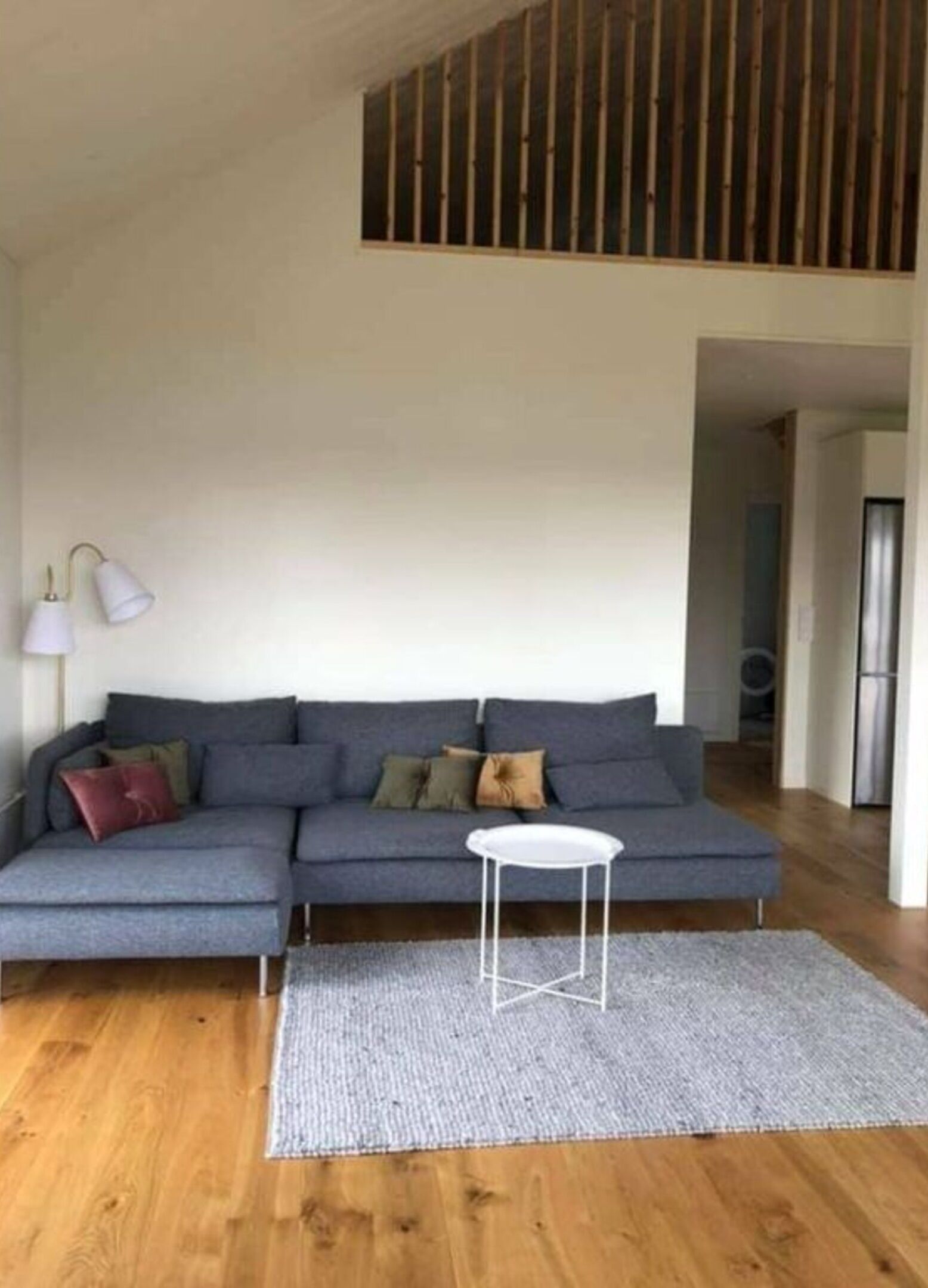 A modern living room with a grey sectional sofa, a small white side table, and a grey rug.