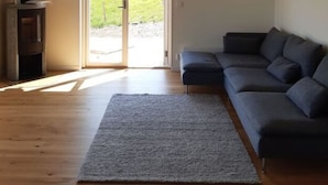 Ein geräumiges Wohnzimmer mit einer großen, grauen Eckcouch, Holzboden und einem Kamin.
