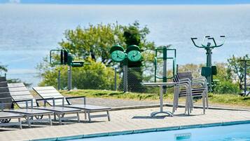 A swimming pool with exercise equipment, lounge chairs, and a view of the sea.