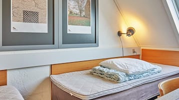 Un dormitorio con cama, mesita de noche, lámpara de pared y cuadros en la pared.