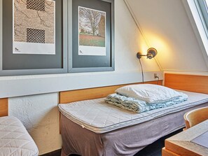Un dormitorio con cama, mesita de noche, lámpara de pared y cuadros en la pared.