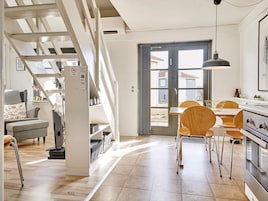 Et moderne køkken med spiseplads, træstole og en trappe, der fører op til et loft.