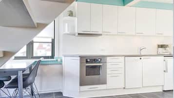 A modern kitchen with white cabinets, a built-in oven, and a coffee machine.