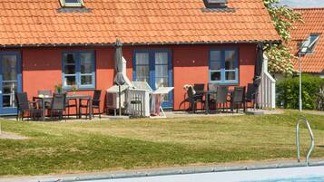 Ein Gebäude mit rotem Dach und vielen Fenstern, einem Schwimmbecken und Sitzgelegenheiten im Freien mit Sonnenschirmen.
