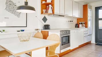 Una cocina moderna con armarios blancos, encimera de madera y una zona de comedor con una mesa blanca y sillas de madera.
