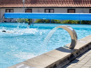 Una piscina con una fuente de agua curva y un borde empedrado.