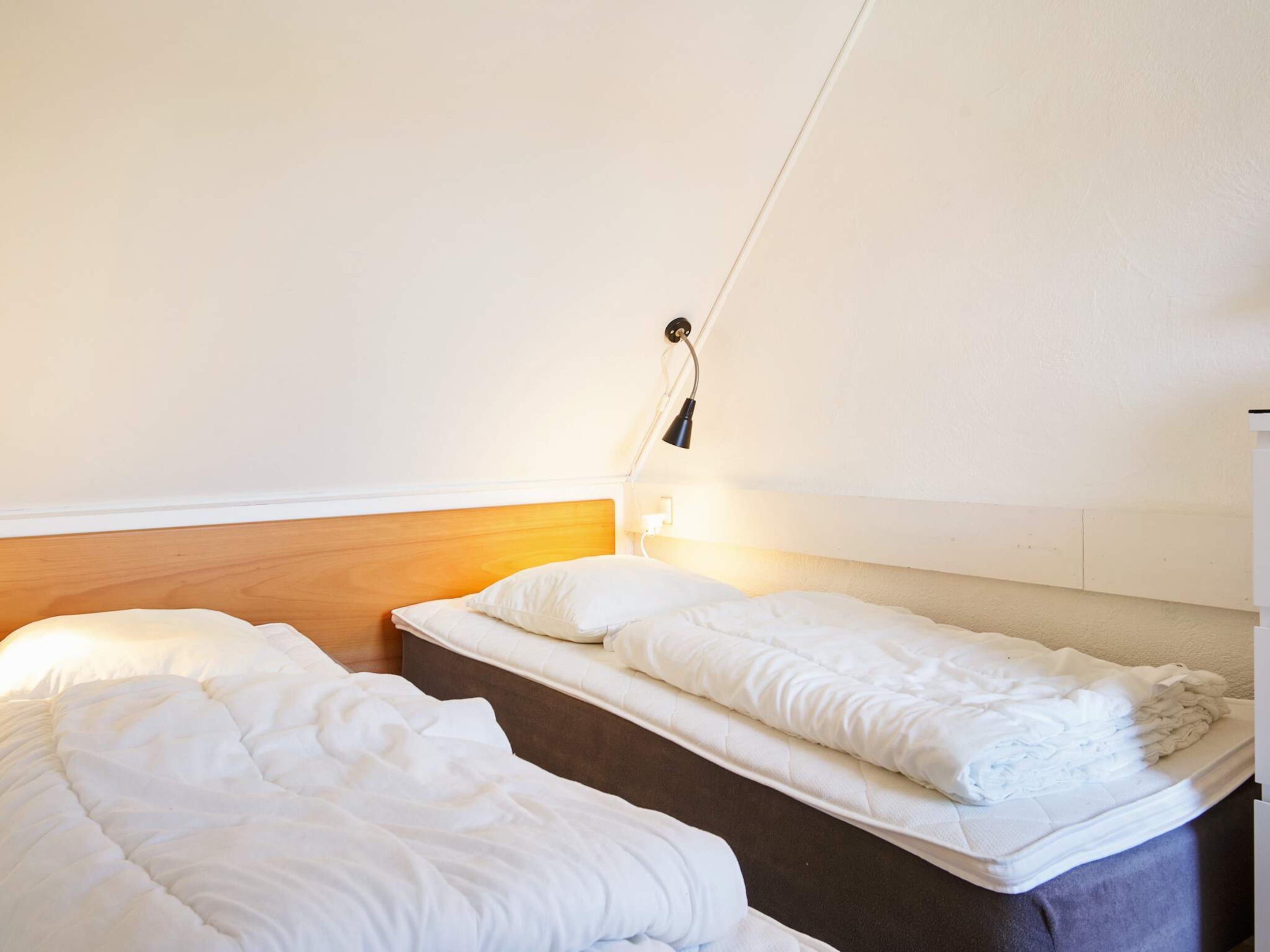 Una habitación pequeña y limpia con dos camas individuales, cabecero de madera y una lámpara de noche.