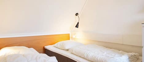 Une petite chambre propre, avec deux lits simples, une tête de lit en bois et une lampe de chevet.
