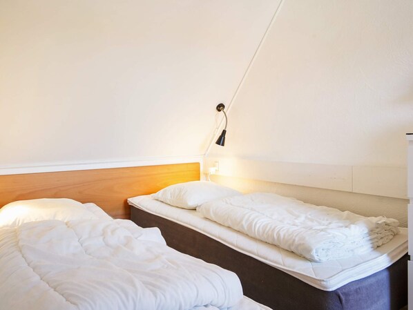 Una habitación pequeña y limpia con dos camas individuales, cabecero de madera y una lámpara de noche.