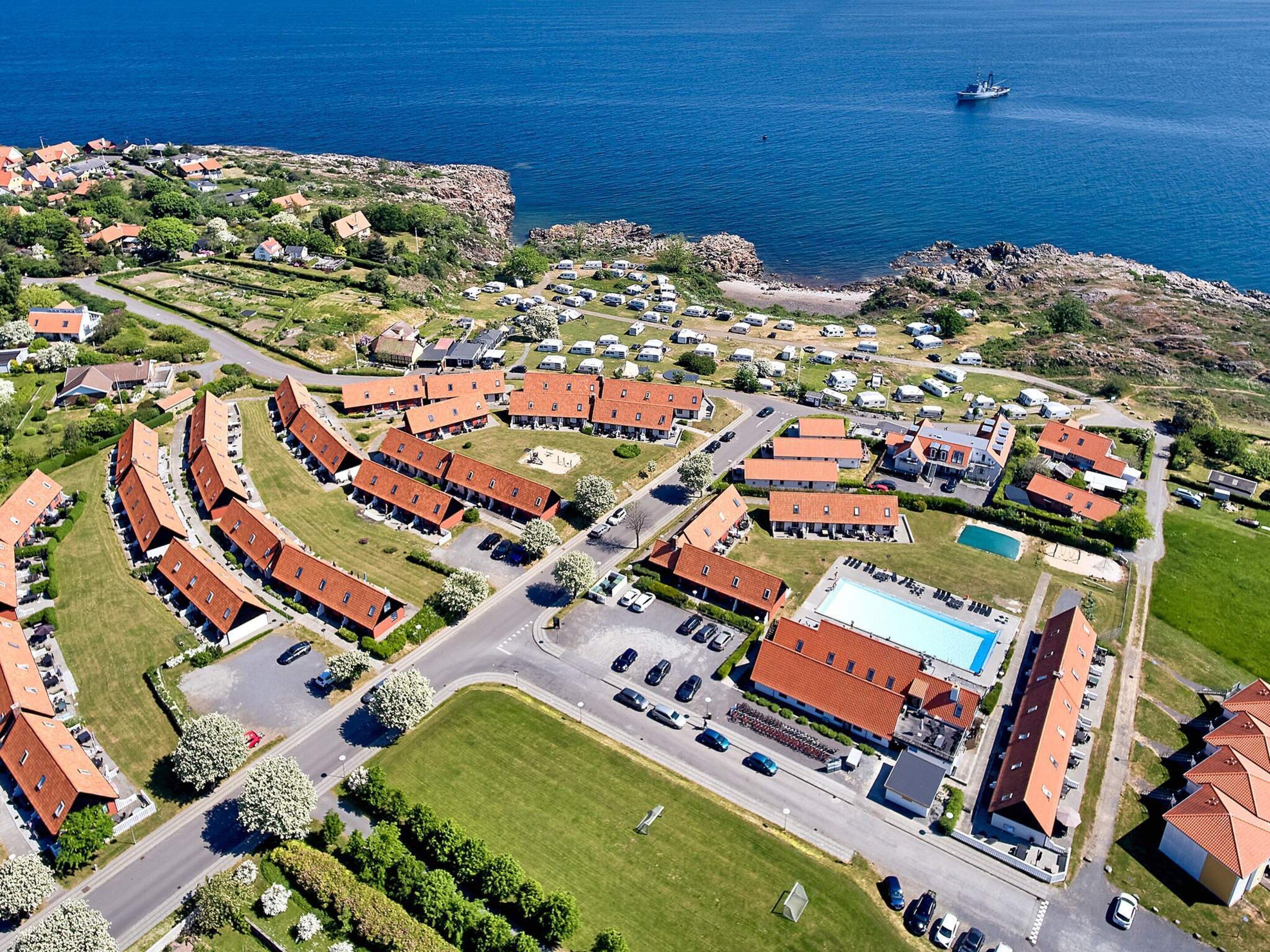 Vue aérienne d’un quartier résidentiel situé sur la côte, avec des maisons à étages, une piscine et un port de plaisance.