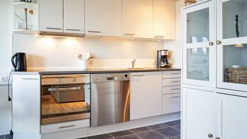 A modern kitchen with white cabinets, a Bosch dishwasher, an oven, and a coffee maker.