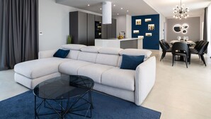 A modern living room with a sectional sofa, a glass coffee table, and a dining area with a chandelier. - Lea Comfortable Holiday Residence (Rasa)