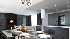 A modern dining area with a long table set for four, a fireplace, and a kitchen in the background. - Lea Comfortable Holiday Residence (Rasa)