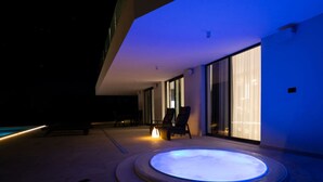 A modern outdoor hot tub area with a circular design, surrounded by a pool and lounge chairs. - Lea Comfortable Holiday Residence (Rasa)