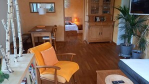 Een gezellige woonkamer met houten vloer, een eethoek met tafel en stoelen, een bank, een televisie en een boekenkast.