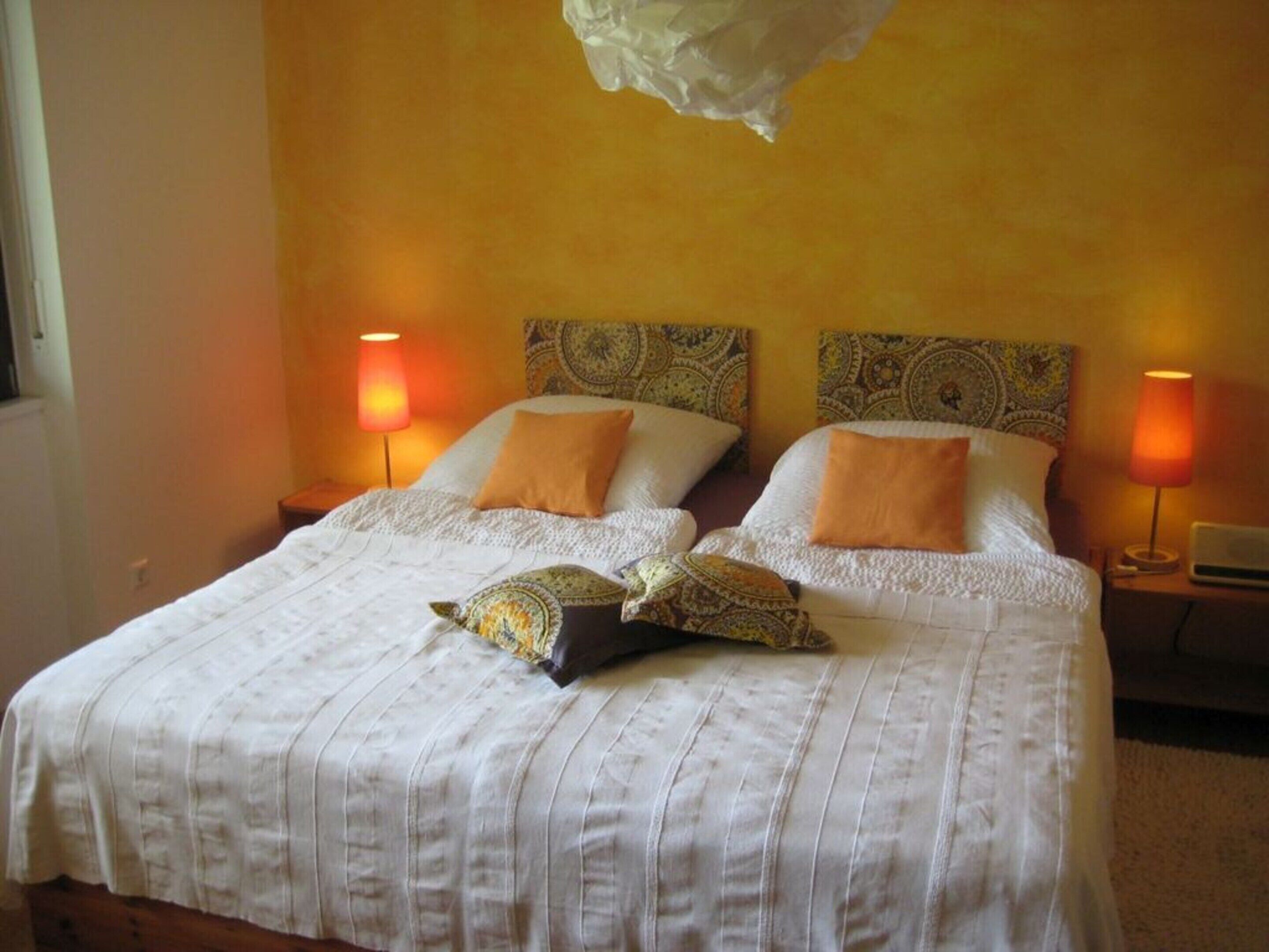 Ein Doppelbett mit weißem Bettbezug und zwei Kissen, zwei Nachttischlampen und gemusterte Kopfteile.
