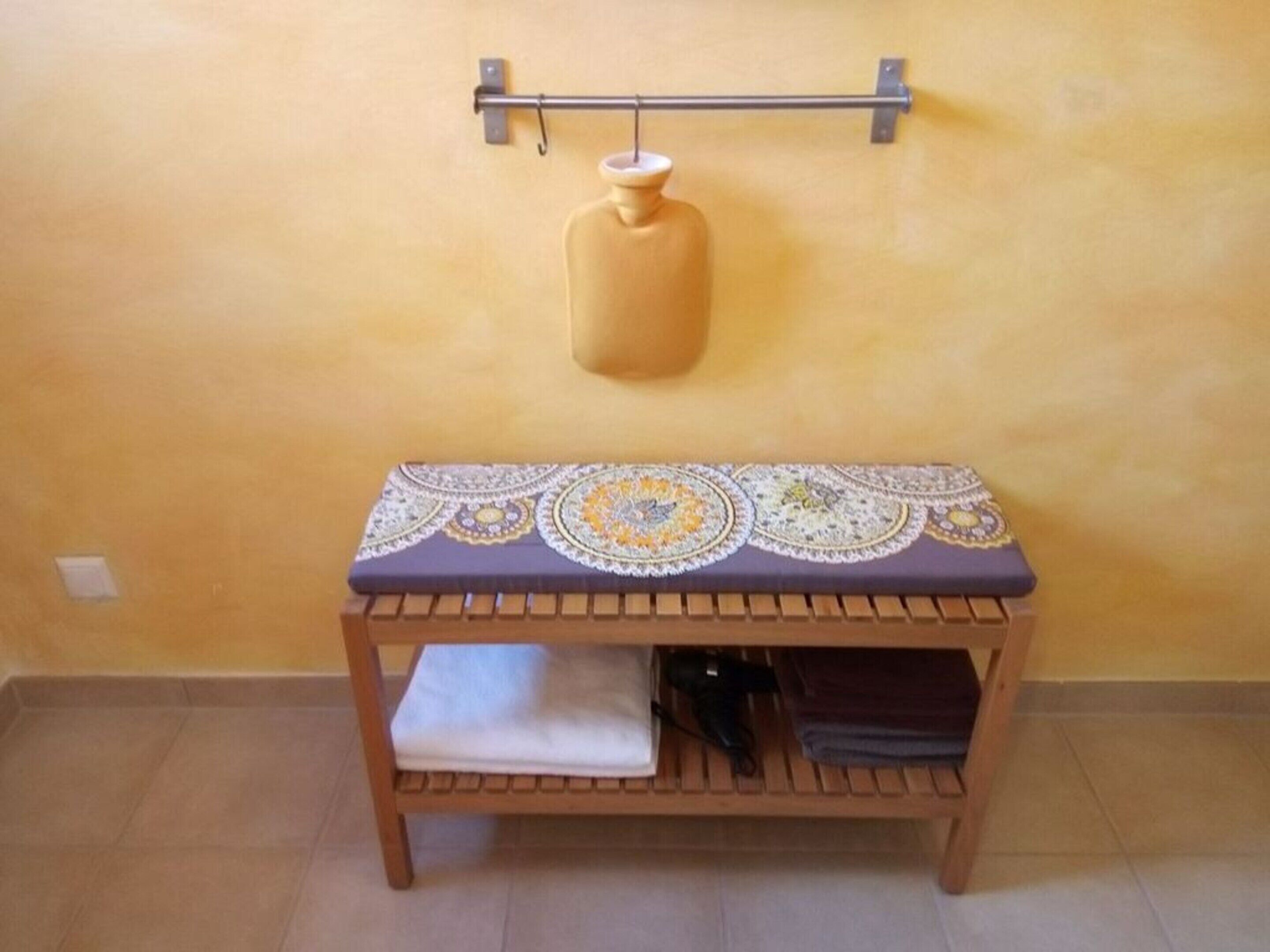 Ein Holztisch mit gemustertem Tischläufer, ein Regal mit gefalteten Gegenständen und ein Wandhaken darüber.