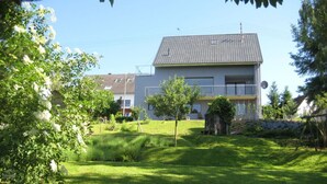 Een modern herenhuis met twee verdiepingen en een pannendak, omgeven door een verzorgd gazon en bomen.
