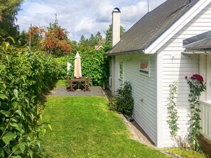 A white house with a garden, a wooden table with chairs, and a white fence.