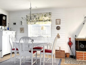Un comedor con mesa y sillas blancas, una araña de cristal, una ventana con vistas y una chimenea.