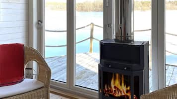 A room with a large window, a wicker chair, a table with candles, and a wood-burning stove.