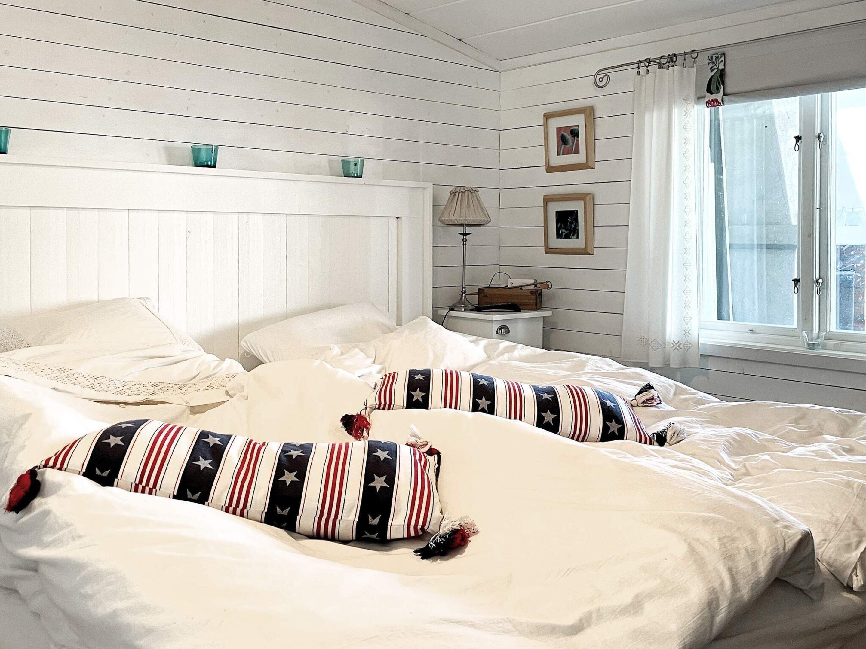A bedroom with a bed, pillows, a nightstand, a lamp, and a window with curtains.