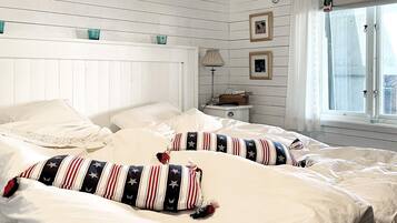 A bedroom with a bed, pillows, a nightstand, a lamp, and a window with curtains.