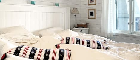 A bedroom with a bed, pillows, a nightstand, a lamp, and a window with curtains.