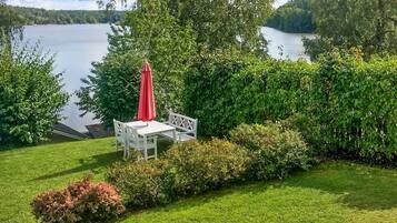 A patio with a table and chairs, a red umbrella, and a view of a lake.