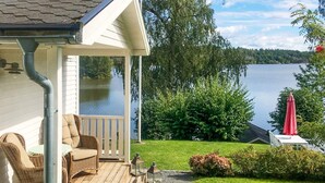 A wooden deck with wicker furniture, a view of a lake, and a red umbrella. - 4 Star Holiday Home in Linkoping (Linkoping)