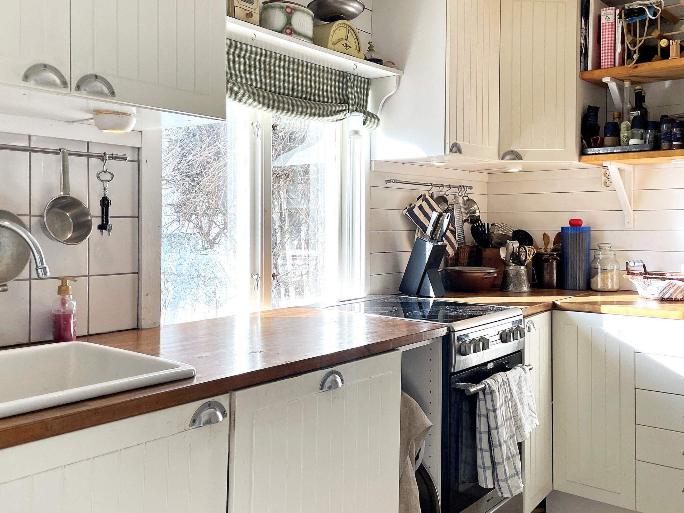 A kitchen with white cabinets, a stove, a sink, and various kitchen utensils.