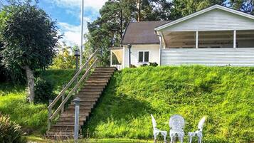 A house with a staircase leading to a covered porch, surrounded by greenery and a stone wall.