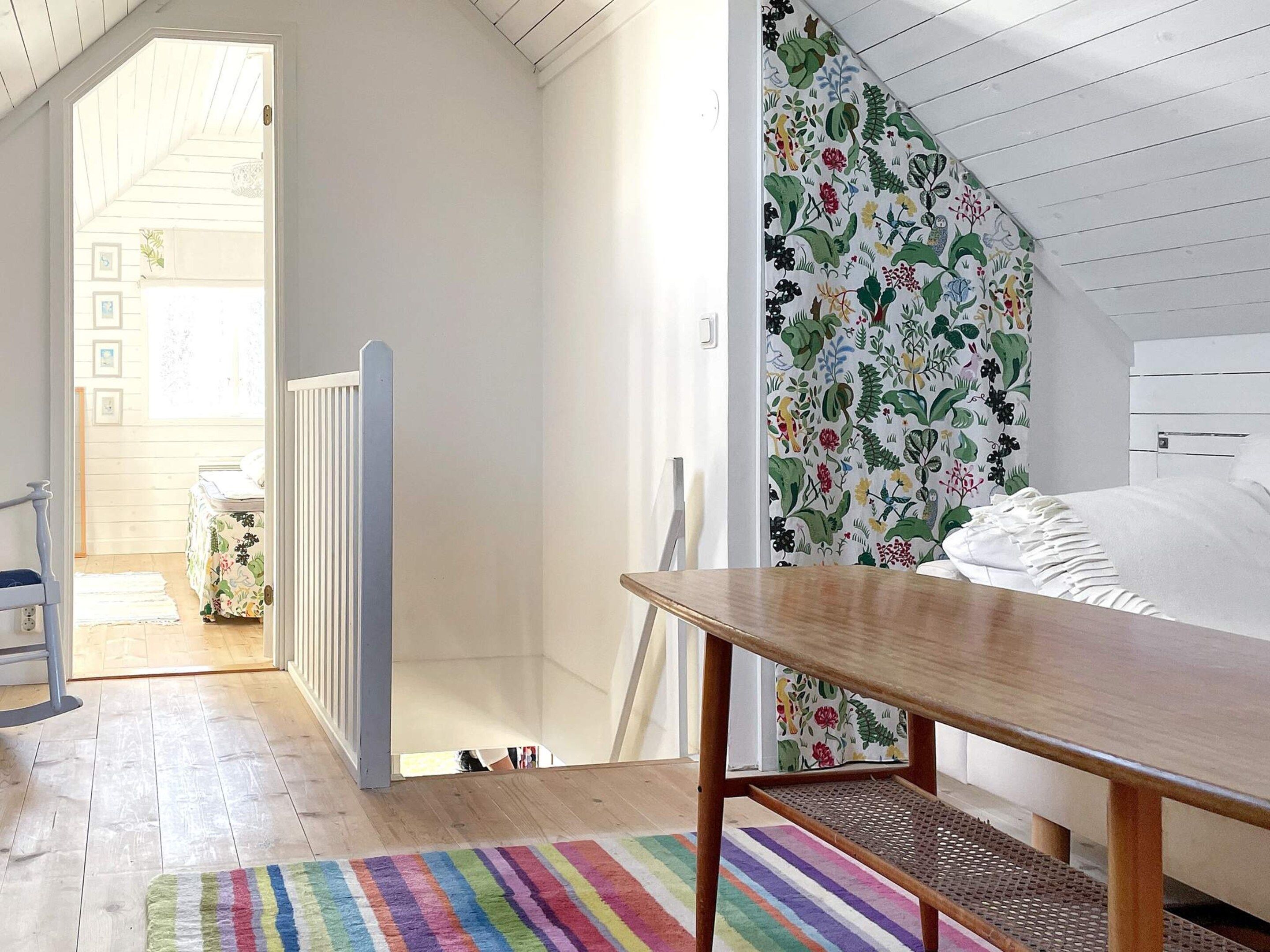 A bedroom with a wooden bed, a colorful striped rug, and a floral-patterned wall.