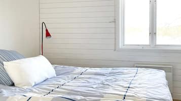 A bed with a striped pillow, a red lamp, and a window with blinds.
