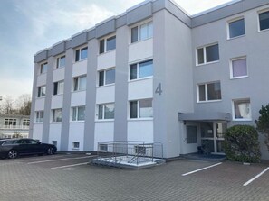 A multi-story residential building with a modern design, featuring a parking area with a covered bicycle rack and a black car parked nearby. - Holiday Apartment Seega (Timmendorfer Strand)