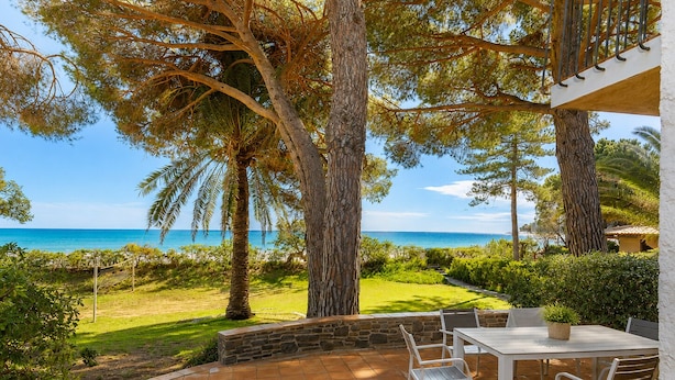 Un patio con mesa y sillas, con vista a una playa con árboles y un cielo despejado.