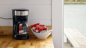 Una cocina con estantes de madera que sostienen platos y cuencos, una cafetera y un ventanal con vista a un lago.