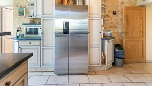 Una cocina con un refrigerador de acero inoxidable de dos puertas, muebles blancos y un fondo de pared de piedra.