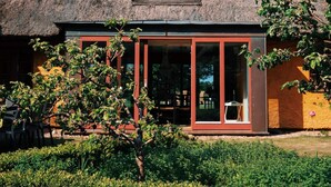 A thatched-roof building with large windows and a tree in the foreground. - 12 Person Holiday Home in Bastad-by Traum (Bastad)