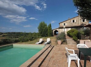 A stone building with a swimming pool, outdoor seating, and a view of the countryside.