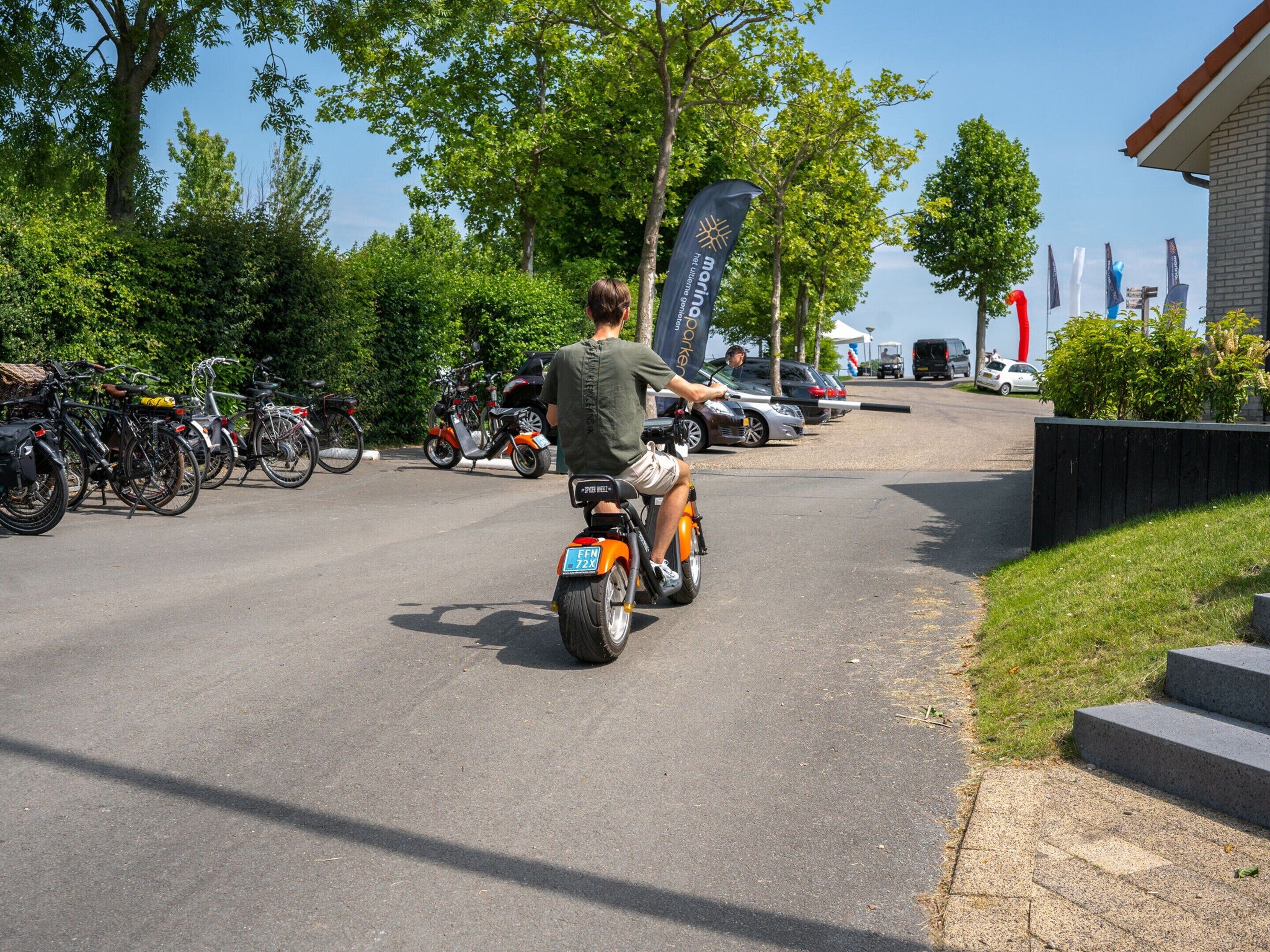 Een man fietst op een kleine, oranje elektrische fiets op een geasfalceerde weg.