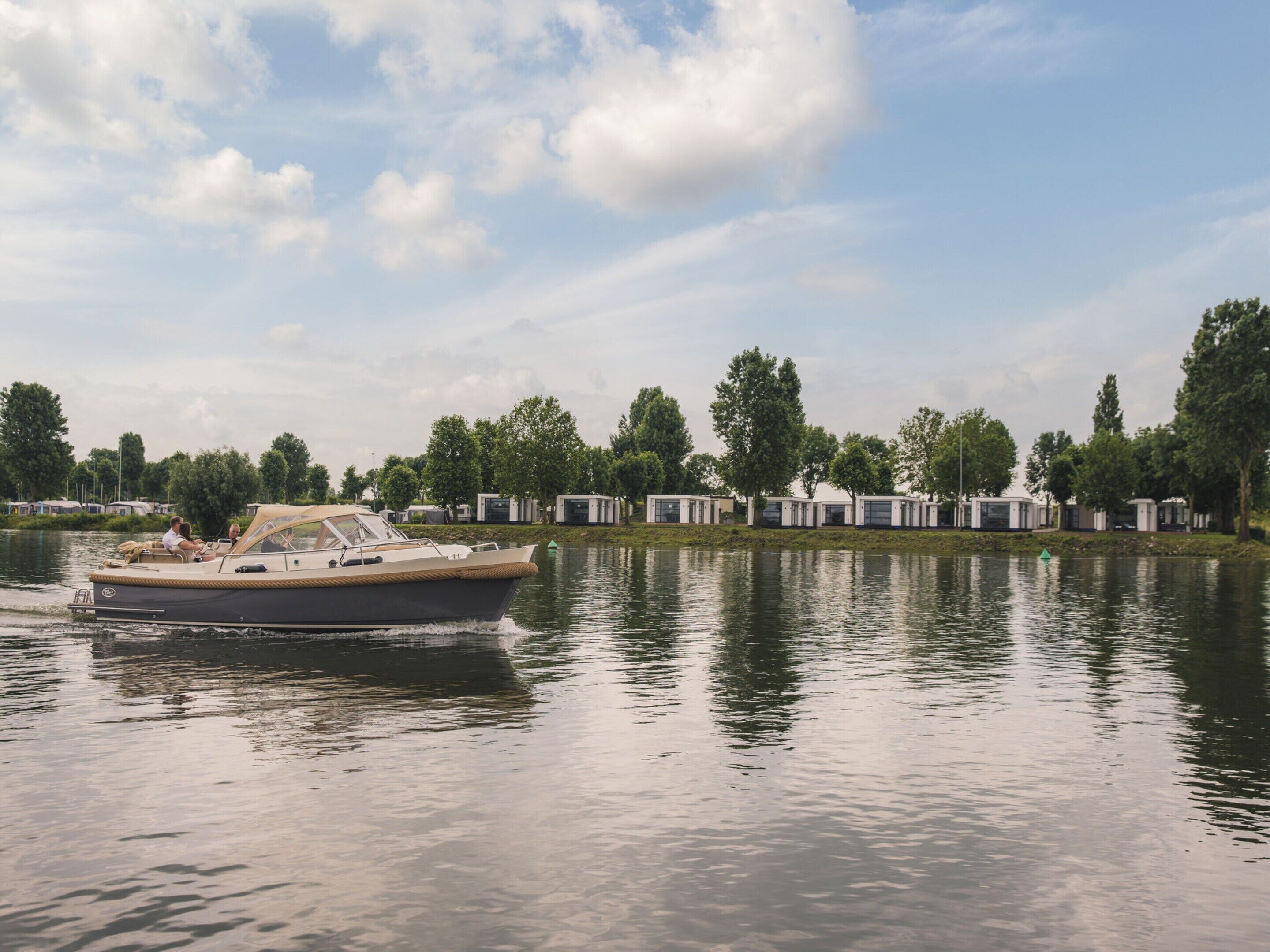 A boat on a calm lake with a row of mobile homes in the background.