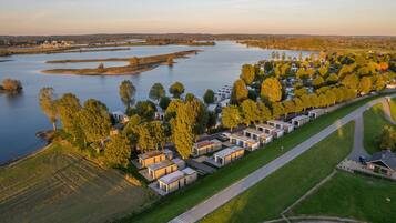 Vista aérea de un parque para vehículos recreativos junto al lago, con filas de vehículos recreativos modernos, una carretera principal y un puente al fondo.