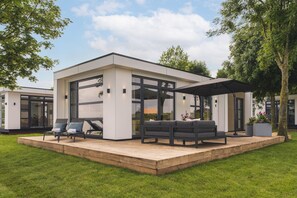 Une maison moderne dotée d’une terrasse, de grandes fenêtres et d’un espace salon extérieur.