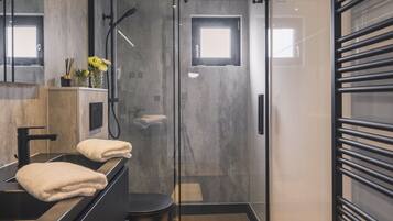 Une salle de bain moderne avec une douche à parois de verre, un meuble-lavabo noir agrémenté d’une serviette et une petite fenêtre.