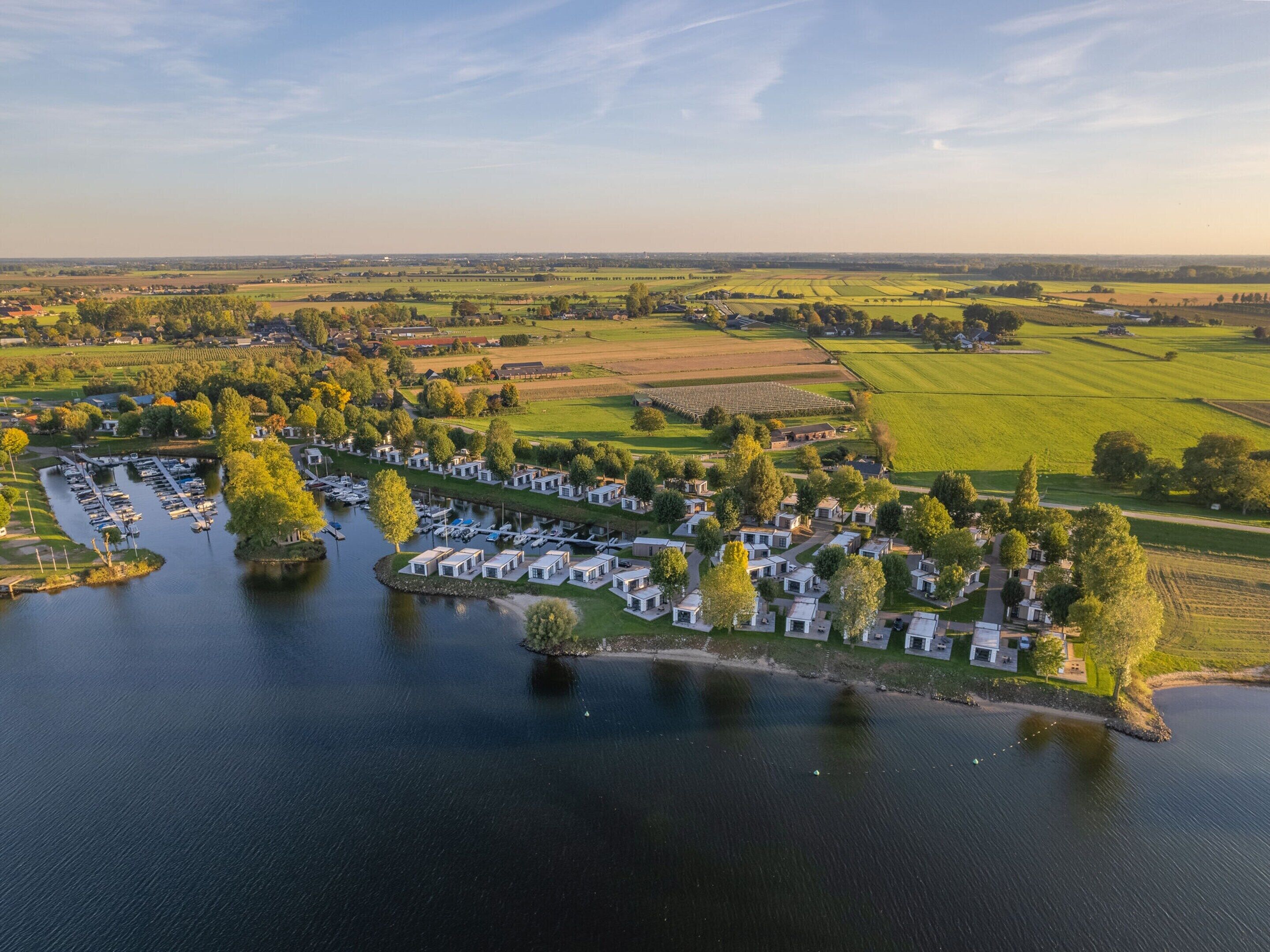 An aerial view of a lakeside campground with RVs and mobile homes, surrounded by fields and trees.