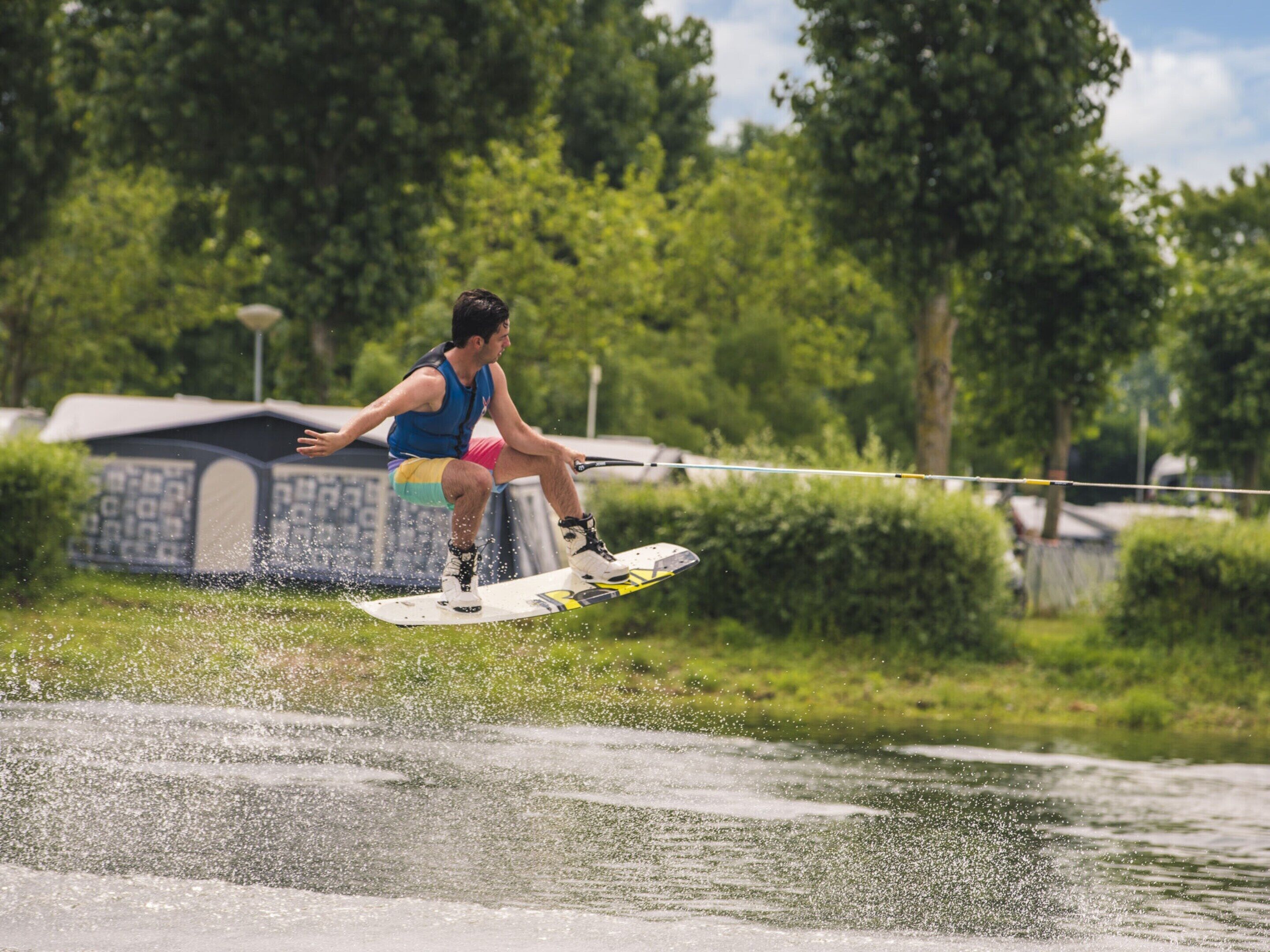 A person wakeboarding on a body of water with a grassy area and trees in the background.