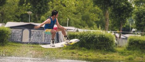 A person wakeboarding on a body of water with a grassy area and trees in the background.