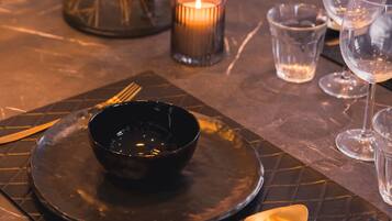 A table set with a black bowl, cutlery, and wine glasses, with a lit candle in the background.