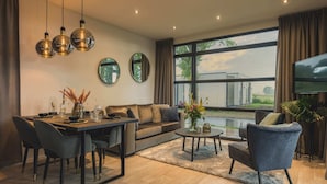 A modern living room with a dining area, large windows, and a flat-screen TV. - Holiday Home in Netherlands With Water Views (Maurik)